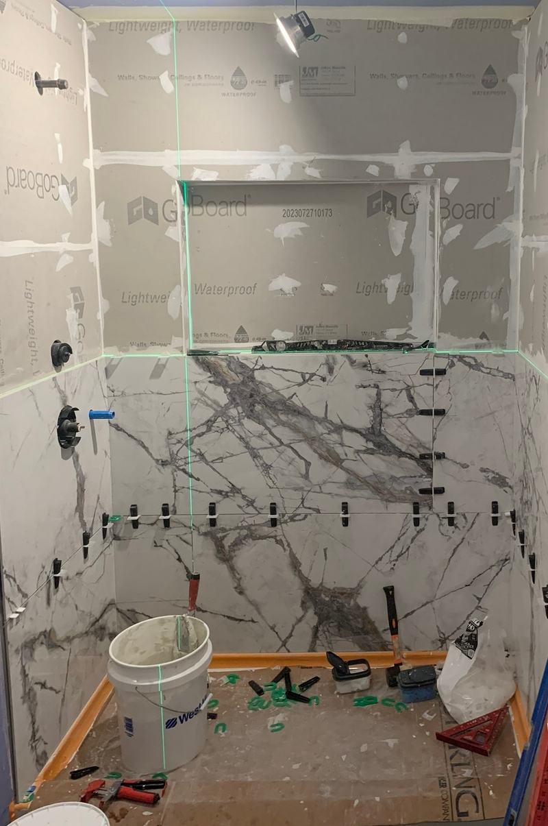 Before: a shower half tiled in white veined tile, with backer board above, leveling clips and tools
