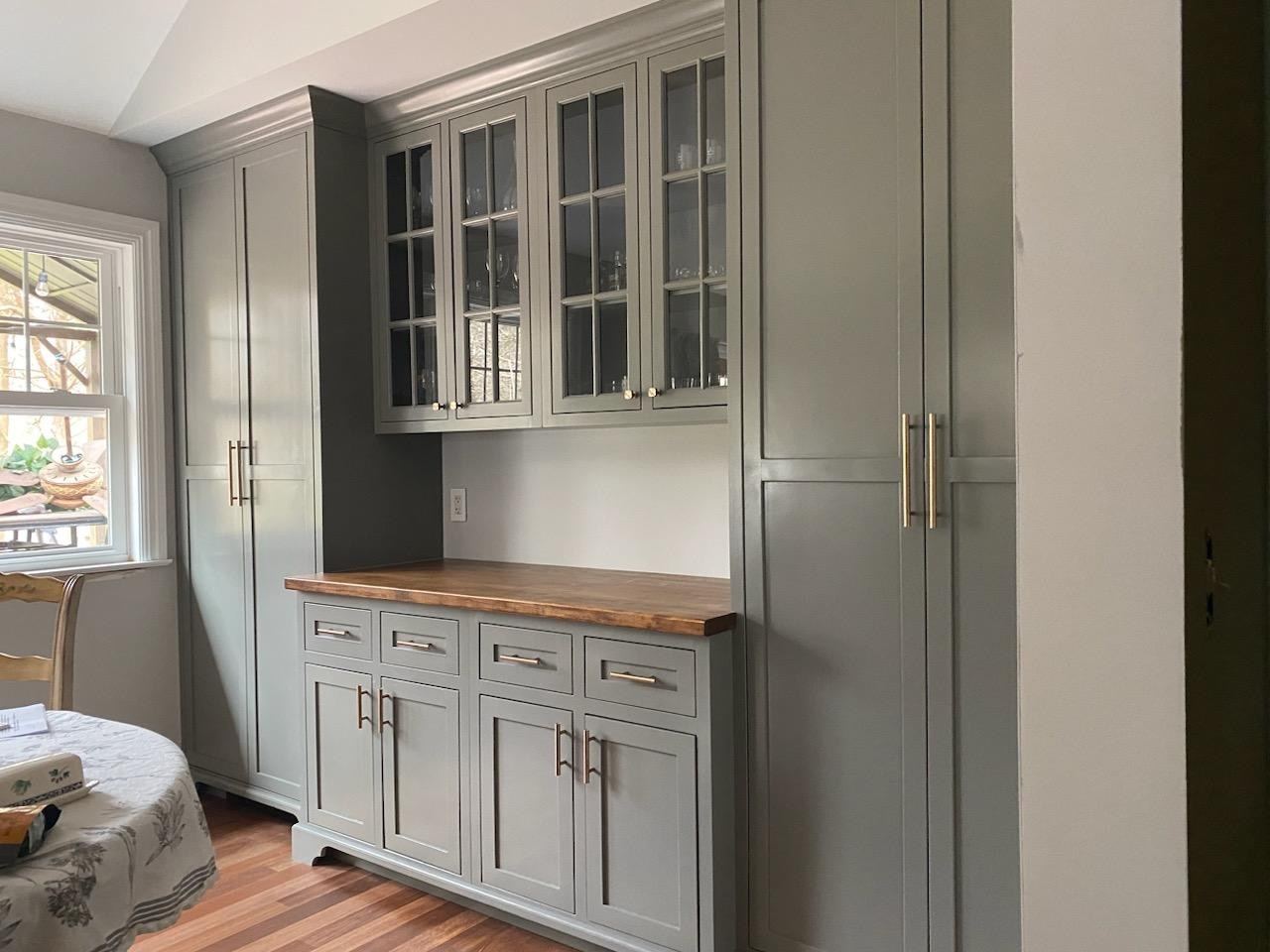 A gray hutch wall: two tall cabinets on either side of glass-front uppers over a wood-topped base with drawers and doors