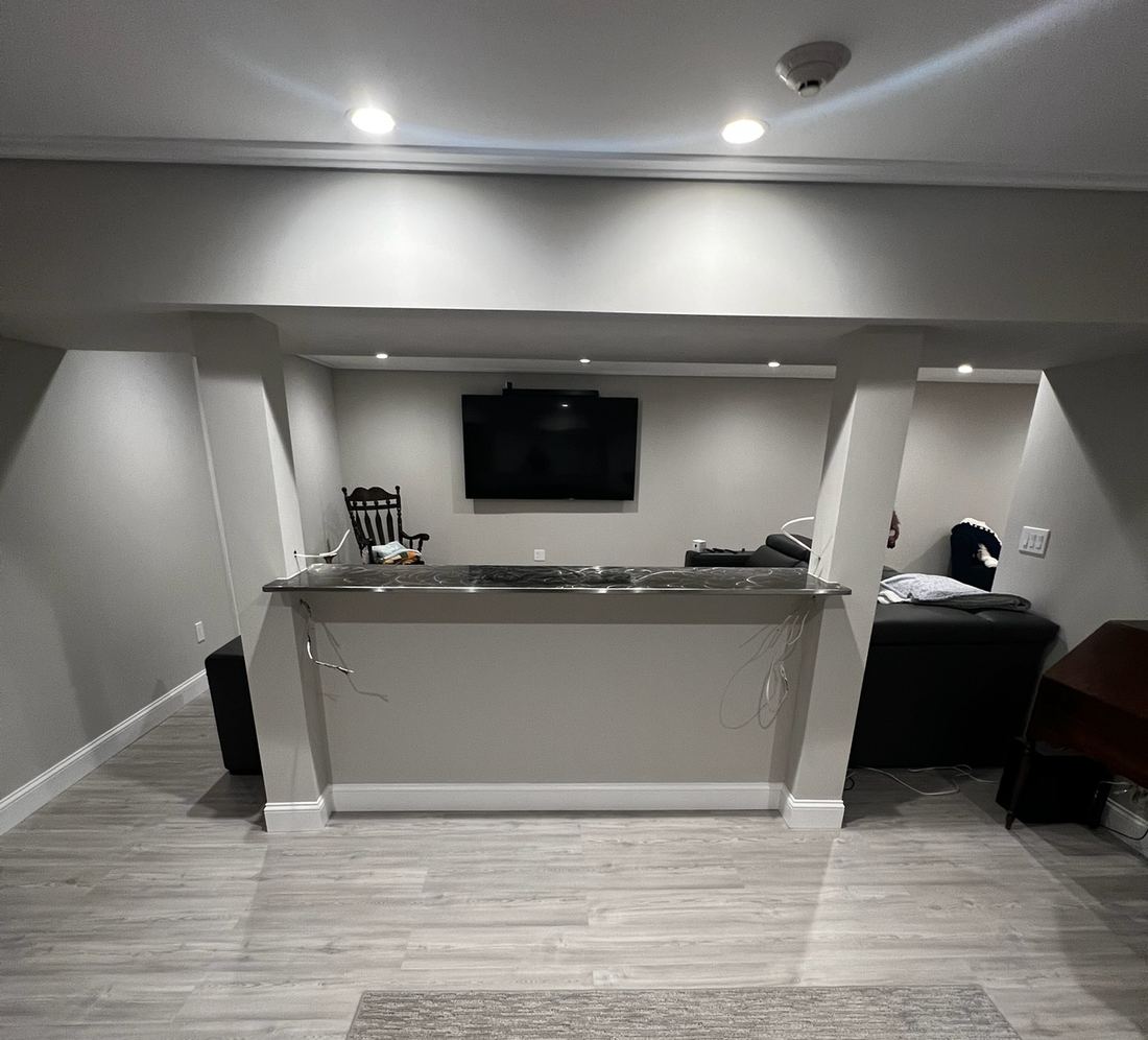 A finished basement: a painted half wall between two wrapped support posts, a TV on the far wall