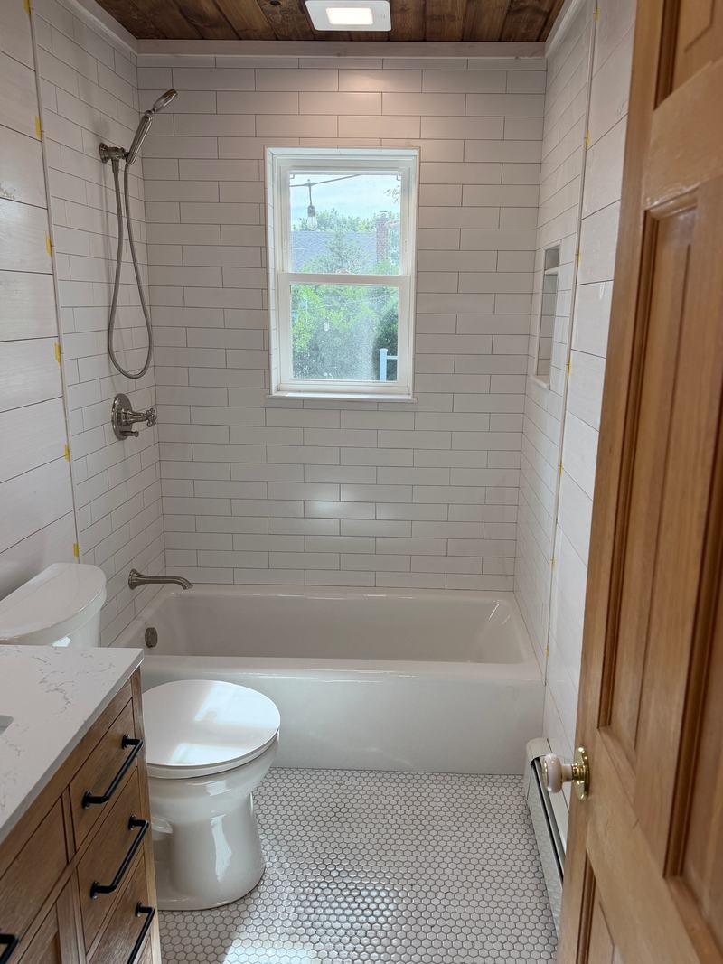 After: the same bathroom with white subway tile, a plank ceiling and a white hexagon mosaic floor