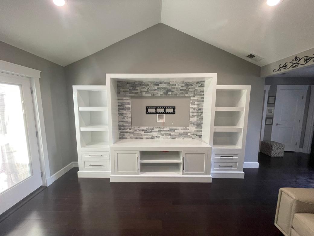 White built-in entertainment wall with open shelves, drawers and doors, installed in a room before the TV was mounted