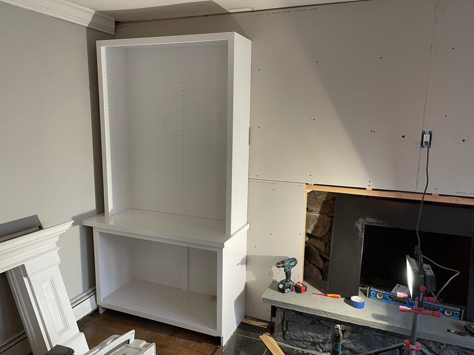 Mid-build: a white bookcase installed beside a fireplace, with tools on the hearth