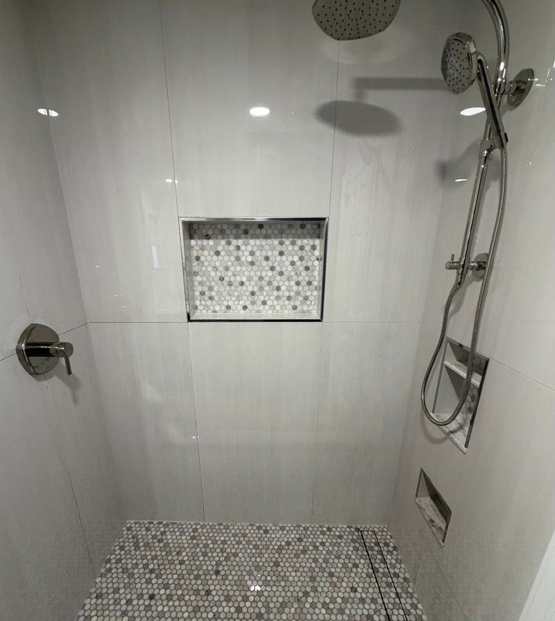 After: the same shower in large light-gray tile, with a mosaic niche