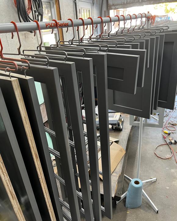 Charcoal-gray cabinet doors hanging in rows on a drying rack in the shop