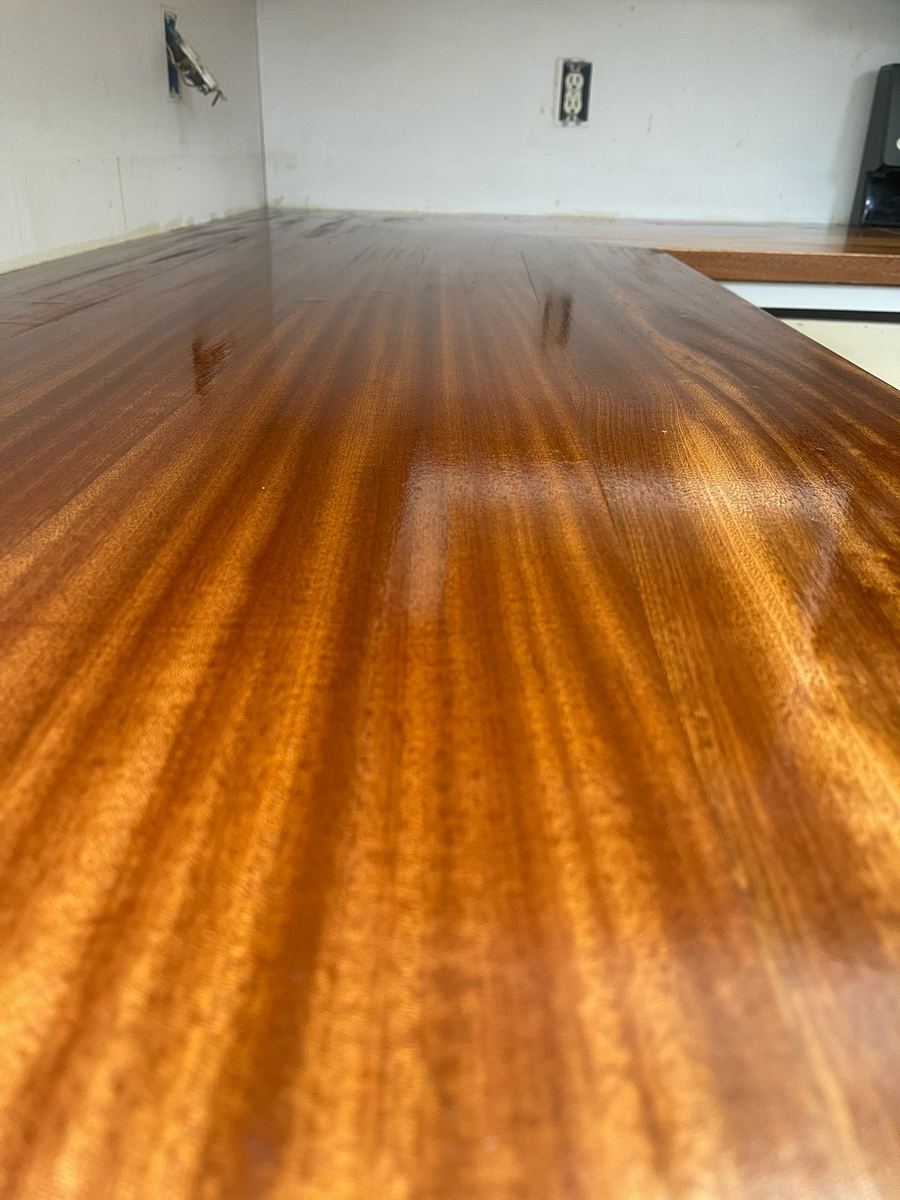 Close-up of a glossy red-brown hardwood countertop with a ribbon grain, turning an L at the far end