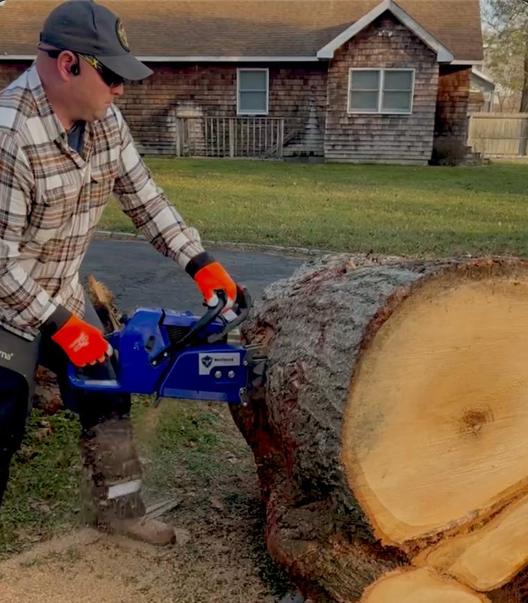 Man in a cap and orange gloves milling a large log with a chainsaw