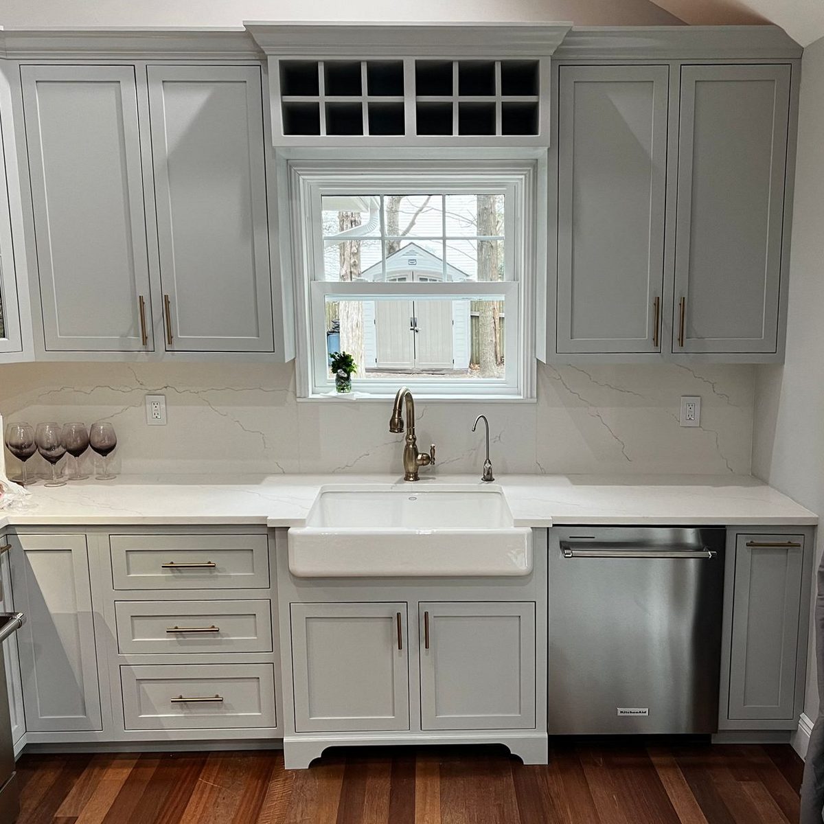 Kitchen sink wall with gray inset cabinets, a wine rack above a window and a white apron-front sink