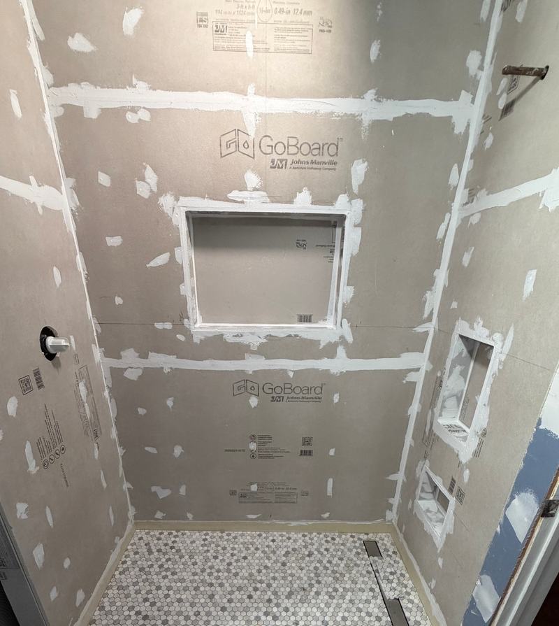Before: a shower with backer board on the walls, a framed niche and a hexagon mosaic floor