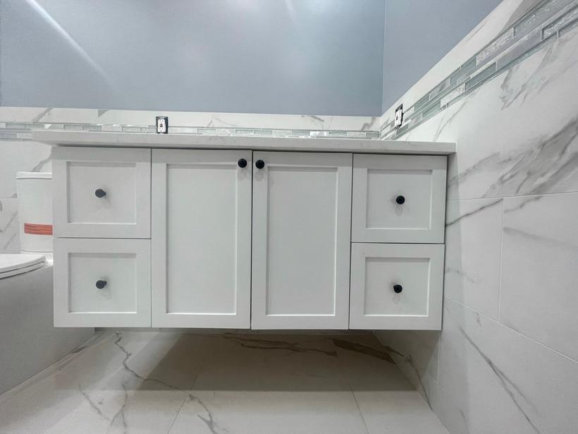Floating white shaker vanity with doors, drawers and black knobs, mounted on a marble-look tiled wall