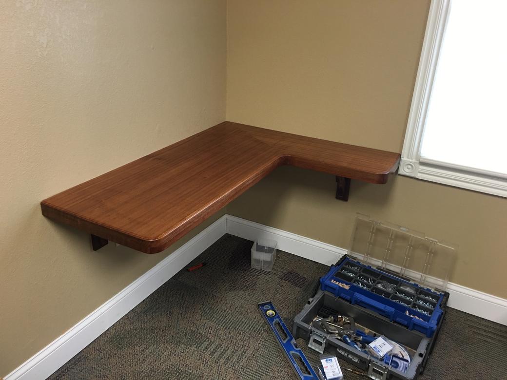 L-shaped wooden desk mounted on brackets in the corner of a room, a toolbox on the floor