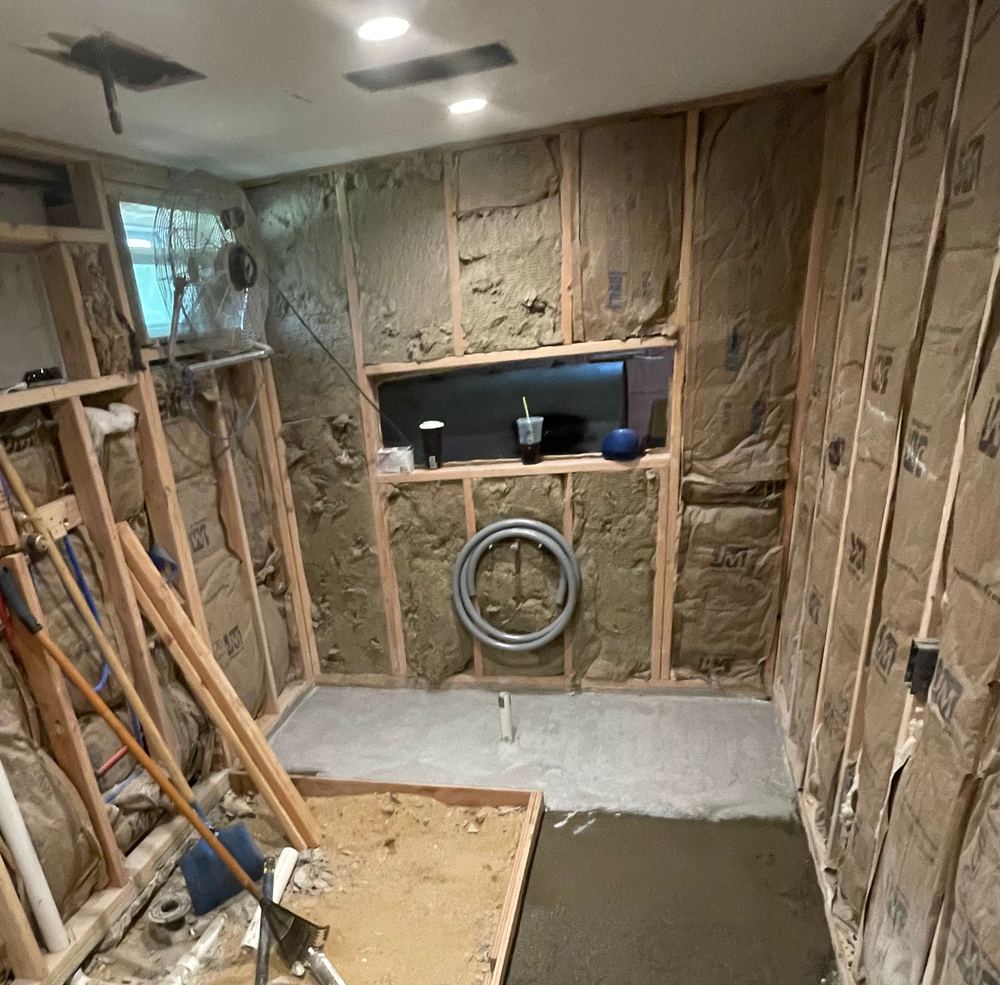 Before: the bathroom gutted to the studs, with open framing, insulation and a niche framed in the far wall