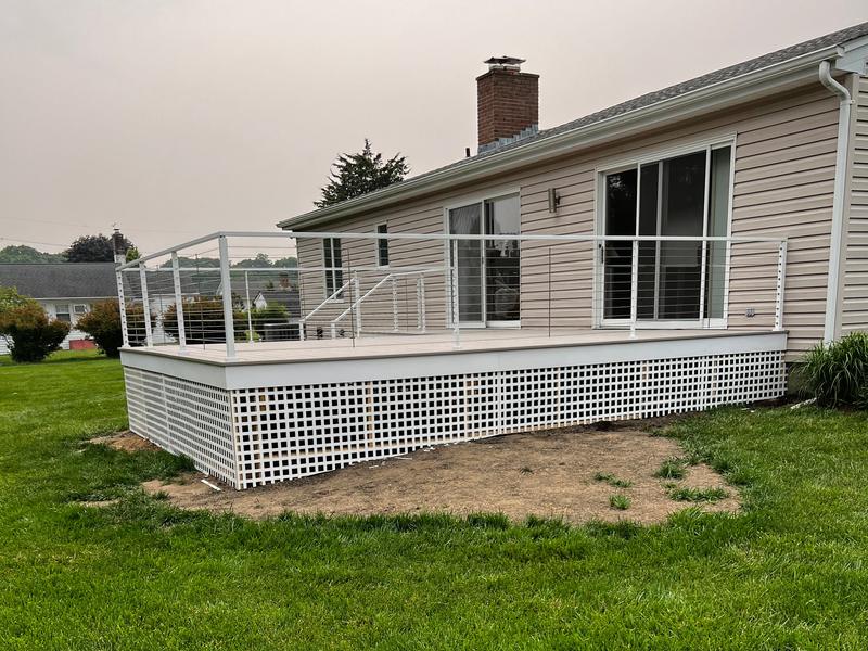 The finished deck with white cable railing and a white lattice skirt