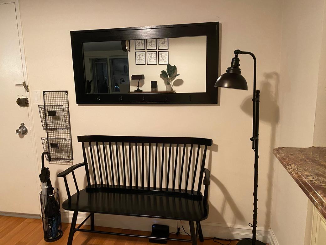 Black-framed entryway mirror with key and coat hooks, hung on an entryway wall